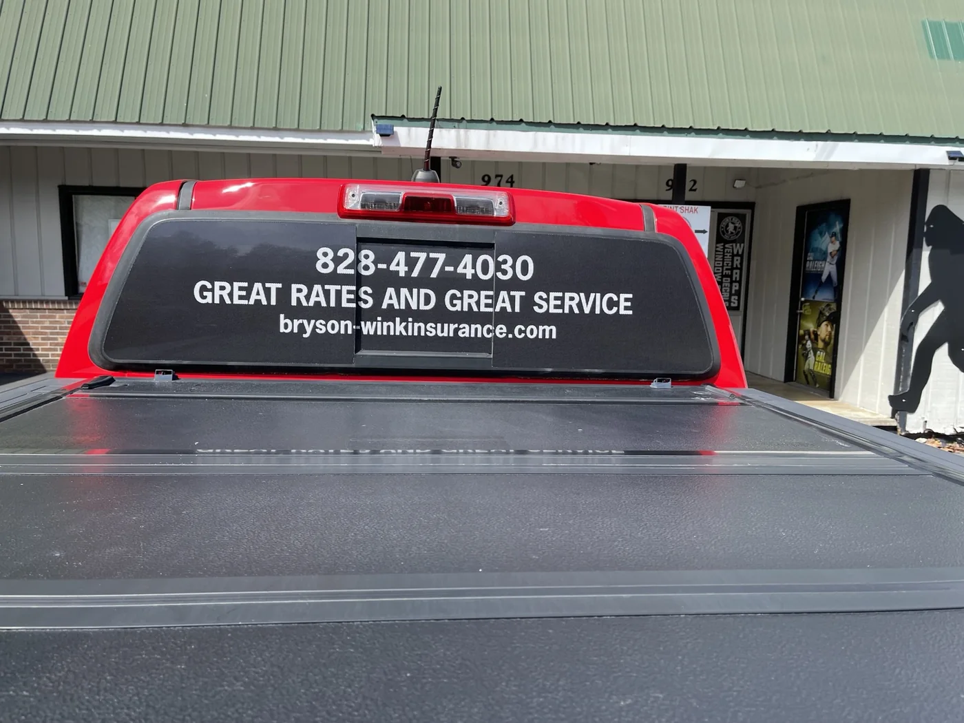 Insurance agency contact information lettered on the back window of a red truck