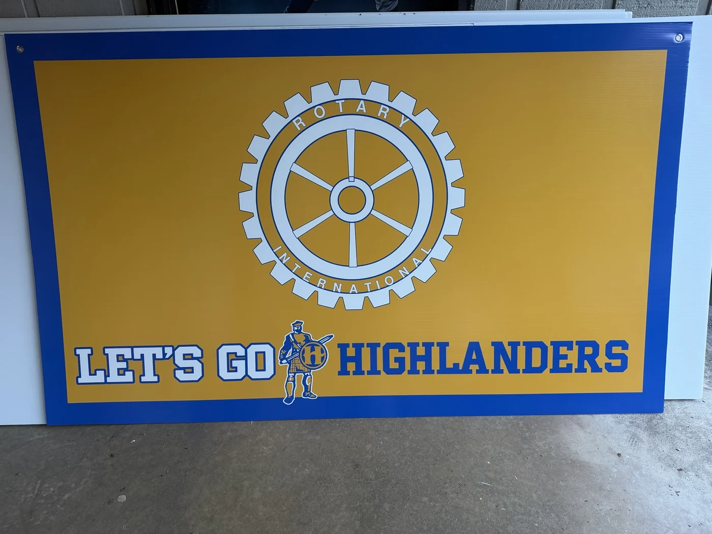 Blue and gold Highlands gym sign with Rotary International emblem and Let’s Go Highlanders lettering