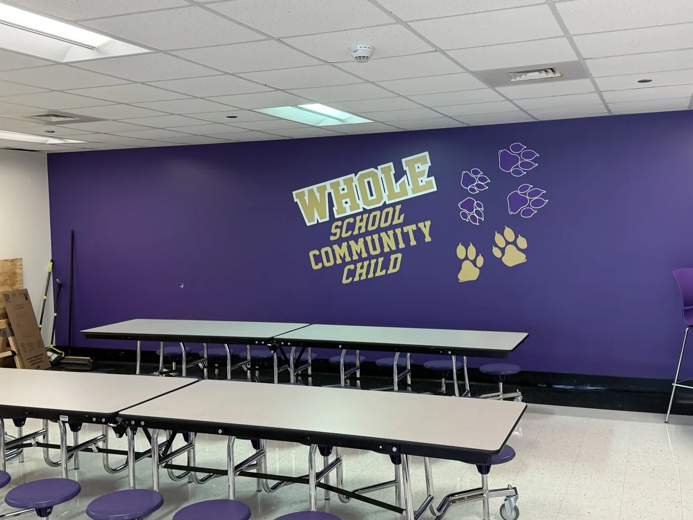 Large school motto and paw print vinyl graphics installed on a purple cafeteria wall