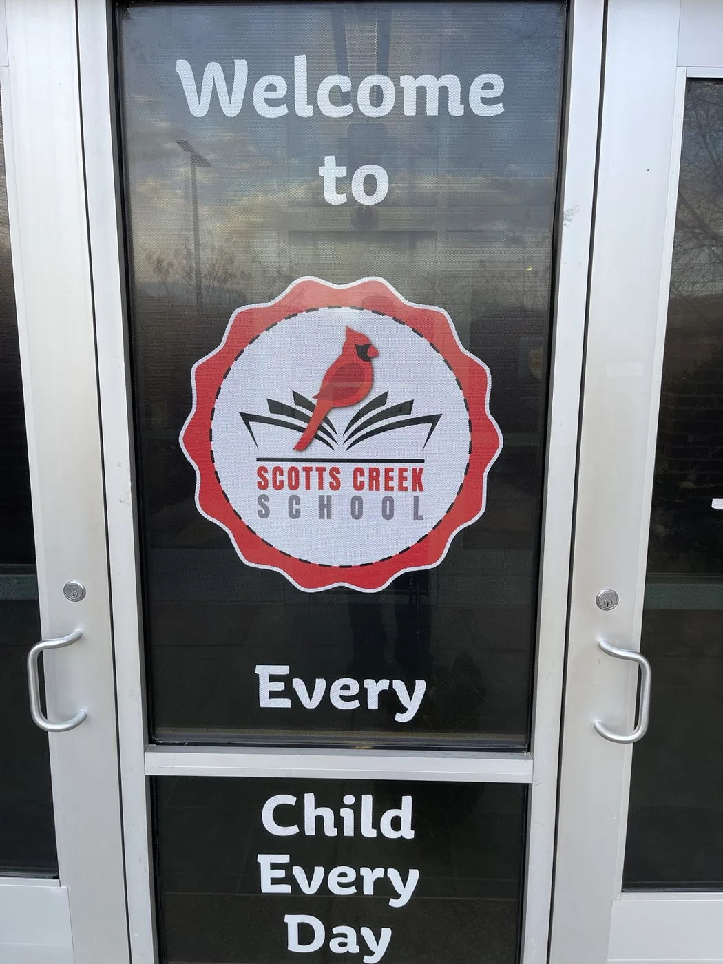 Scotts Creek School cardinal logo and welcome lettering on a glass entry door